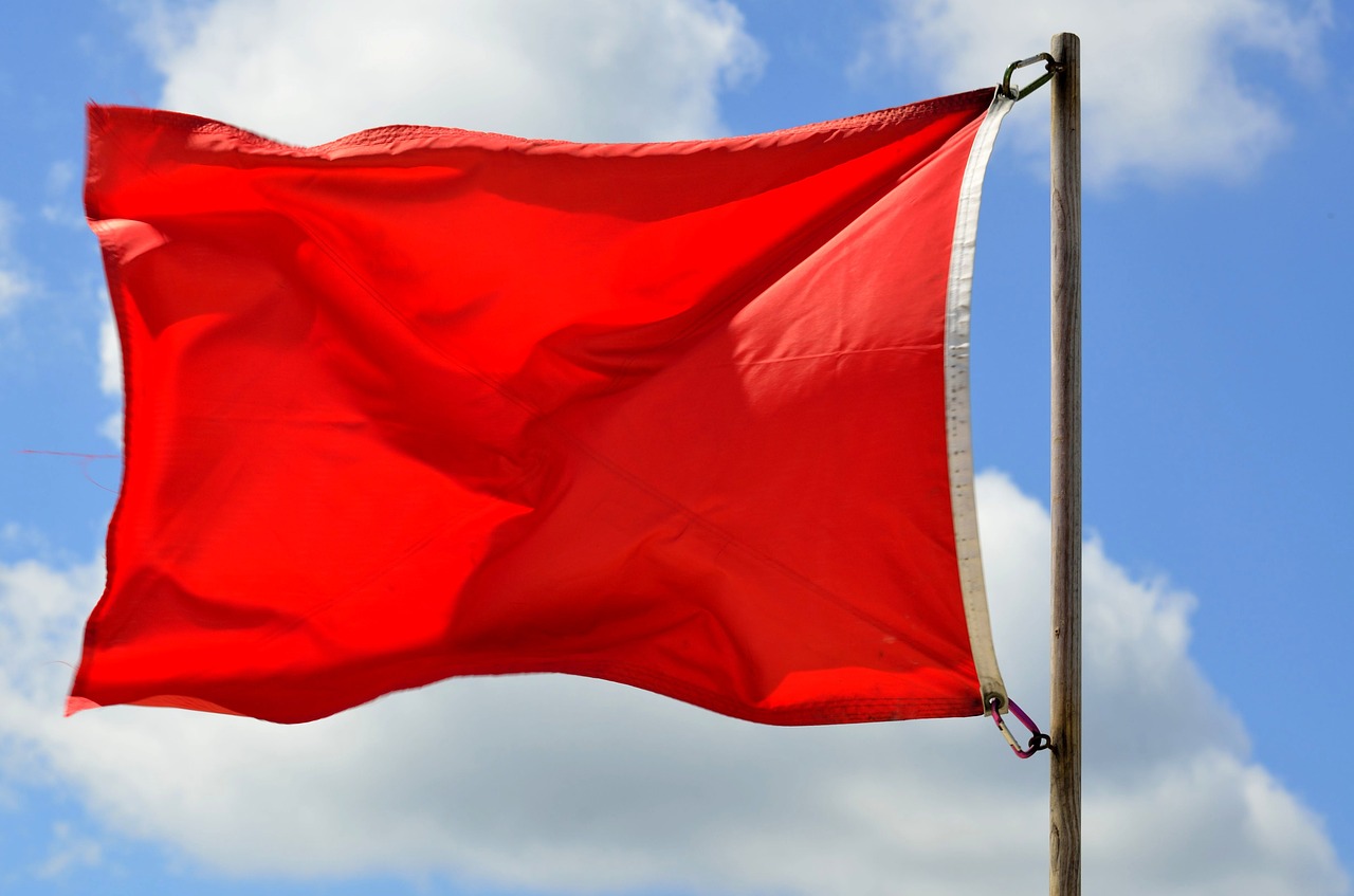 Red flag waving in front of a blue, clouded sky