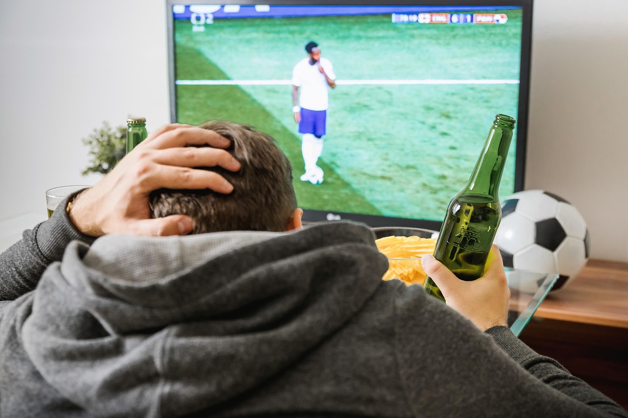Man watching soccer at home with one hand on his head and another holding a beer.